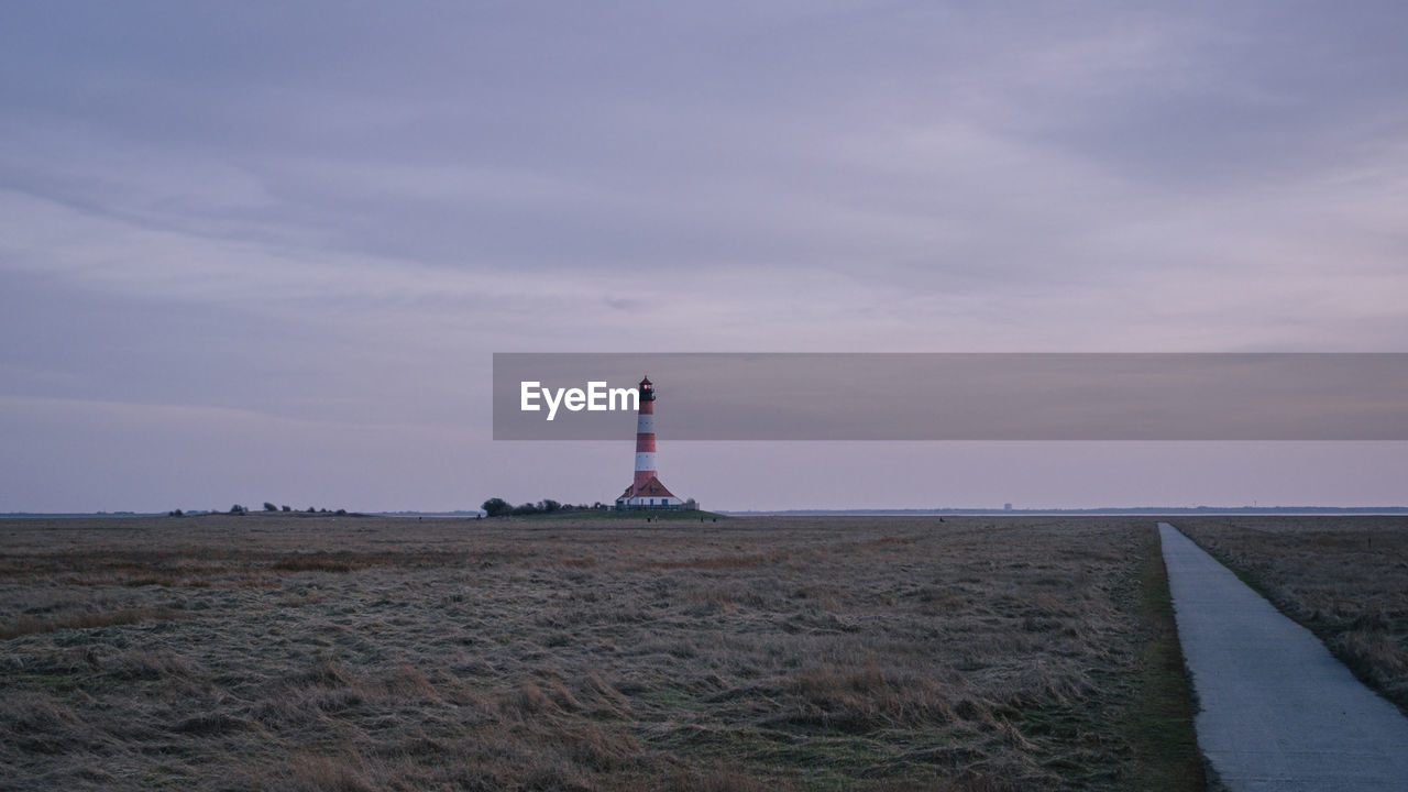 Lighthouse on field by building against sky