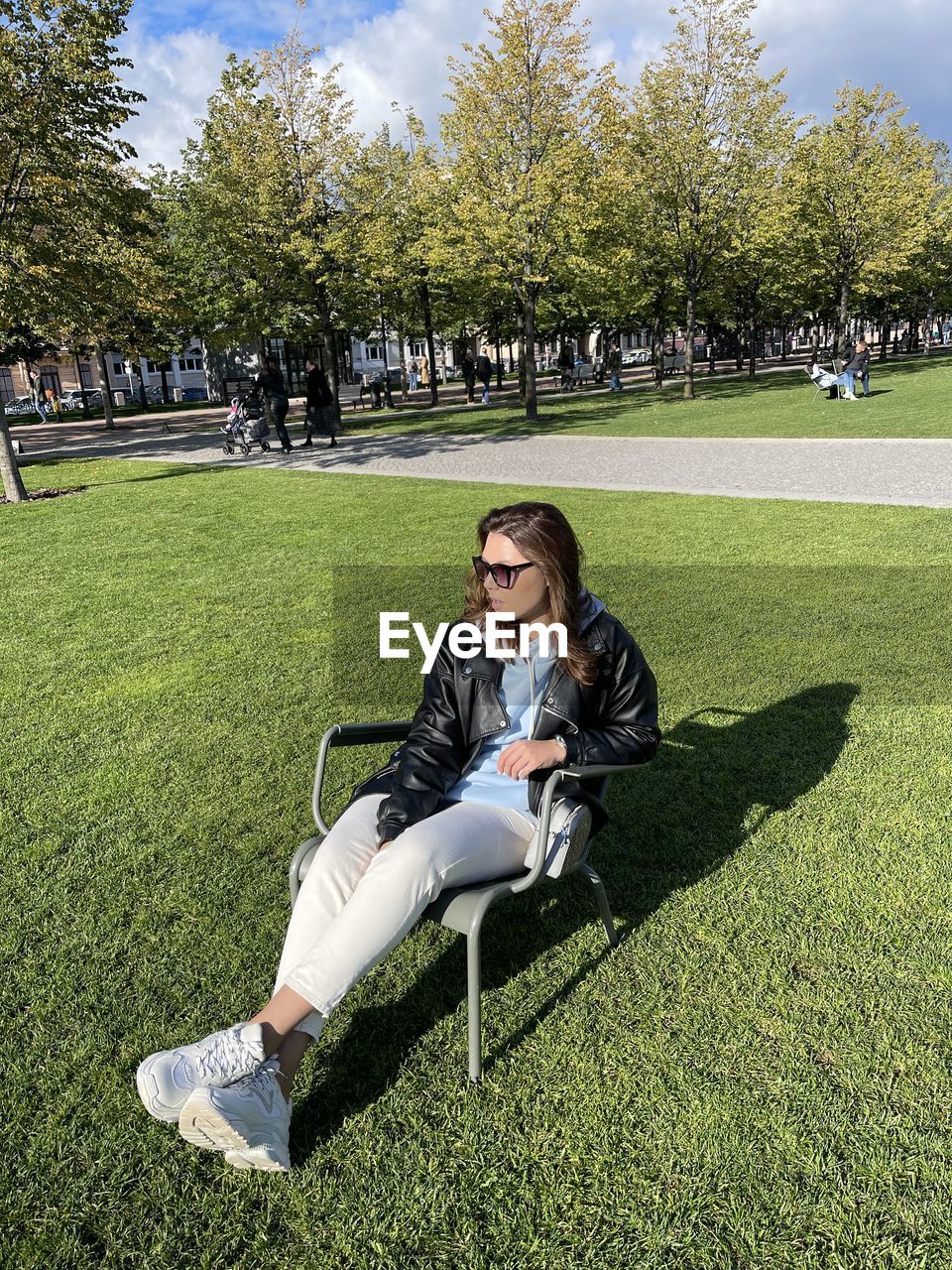 YOUNG WOMAN USING PHONE WHILE SITTING ON PARK