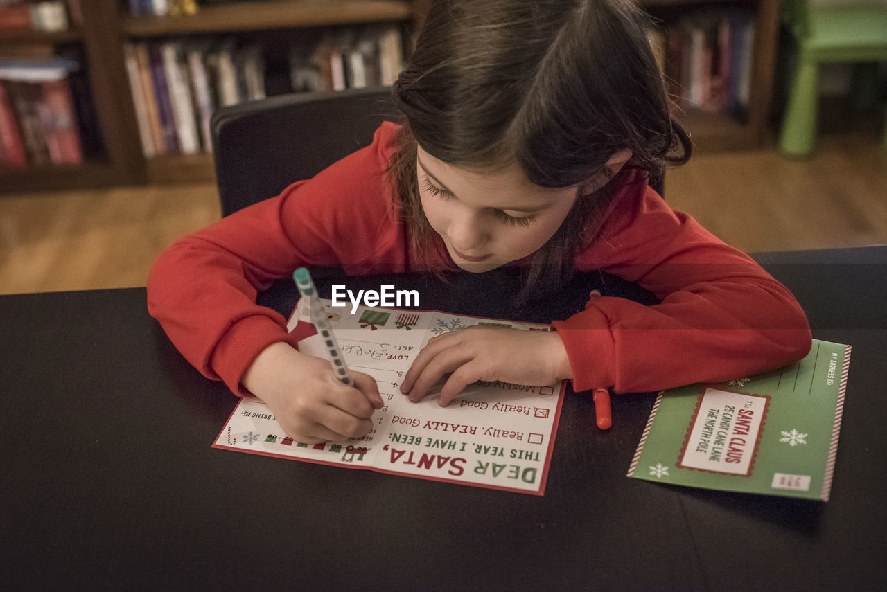 Cute girl writing letter to santa claus at home during christmas