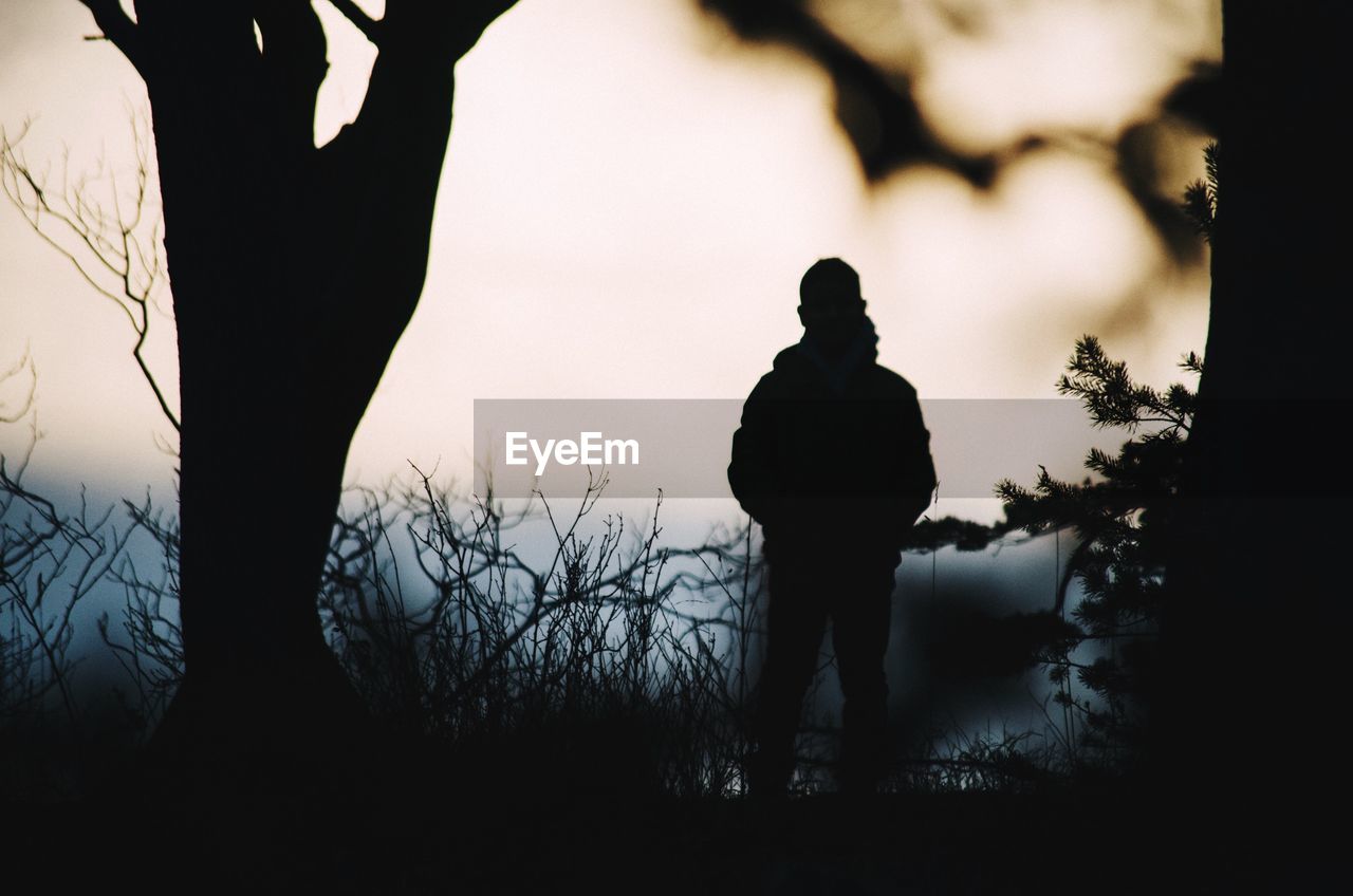 Silhouette man standing on field against sky during sunset