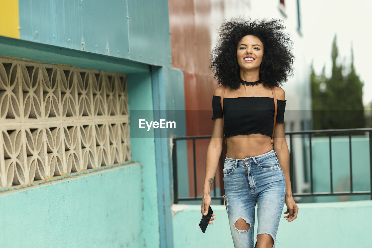 Portrait of smiling young woman walking against wall