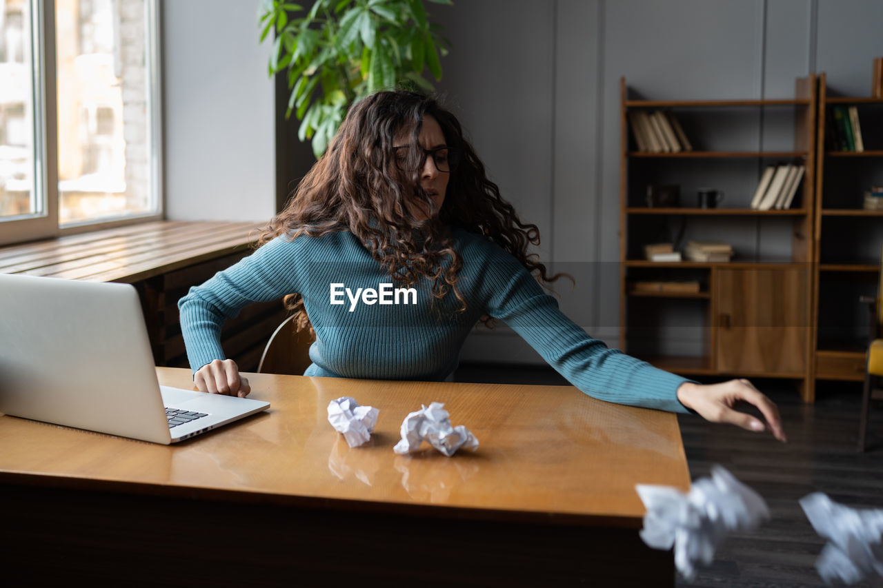 Stressed hysterical young woman throwing crumpled paper, having nervous breakdown at work