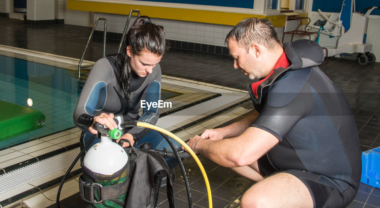 Instructor with woman holding scuba diving equipment at poolside