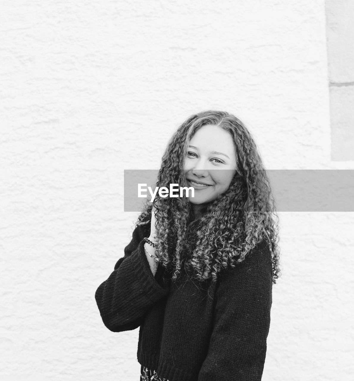 Portrait of smiling young woman with curly hair standing against wall