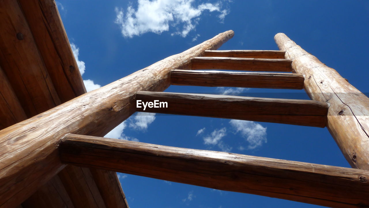 Low angle view of wooden ladder against blue sky