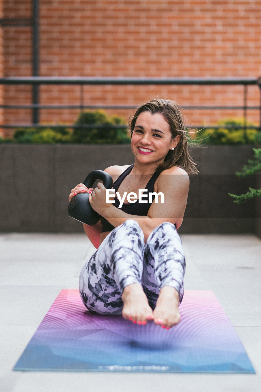 Portrait of a smiling young woman working out outdoors with kettlebell 