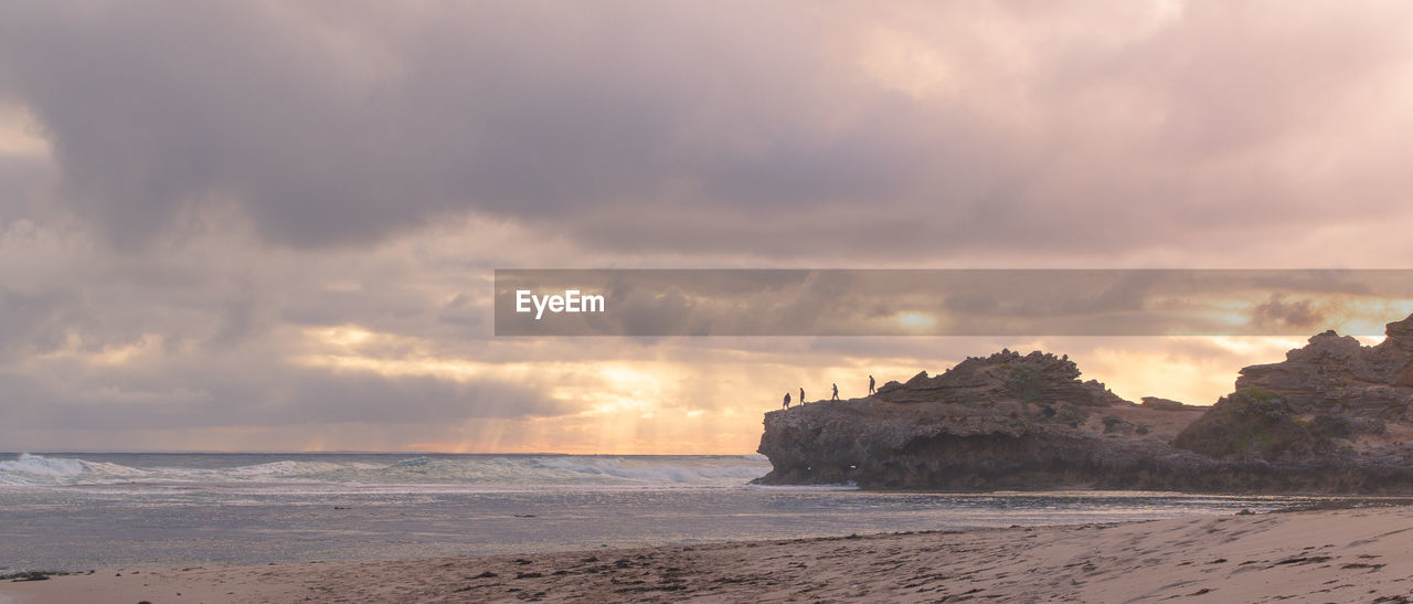 Scenic view of rock formation on shore at beach against cloudy sky during sunset