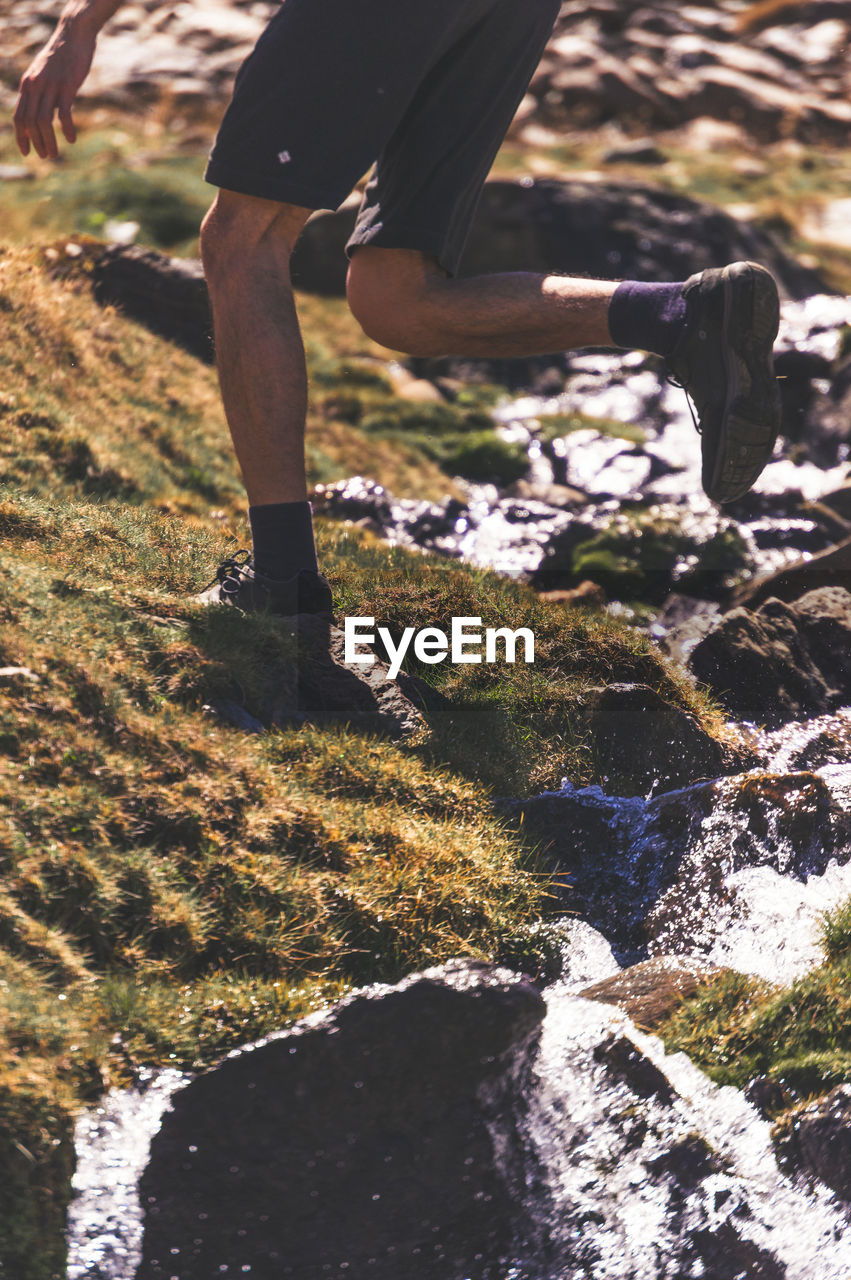 LOW SECTION OF MAN STANDING ON ROCK IN SUNLIGHT