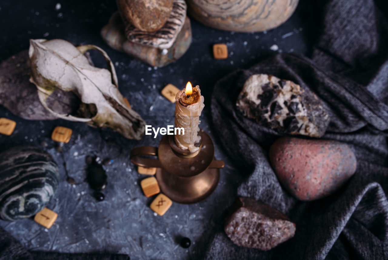 Old dog skull, burning candle, wooden runes and stones on the witch table.