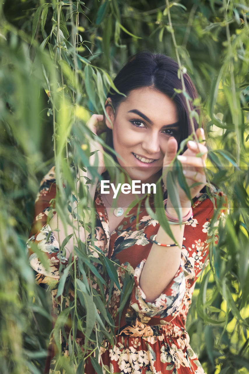 Portrait of playful carefree young woman hiding behind tree leaves