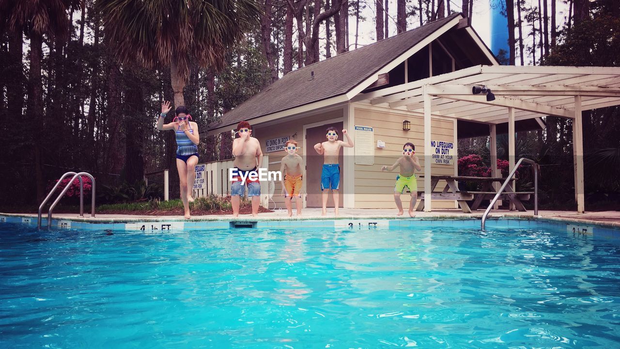 Shirtless friends diving into swimming pool against house