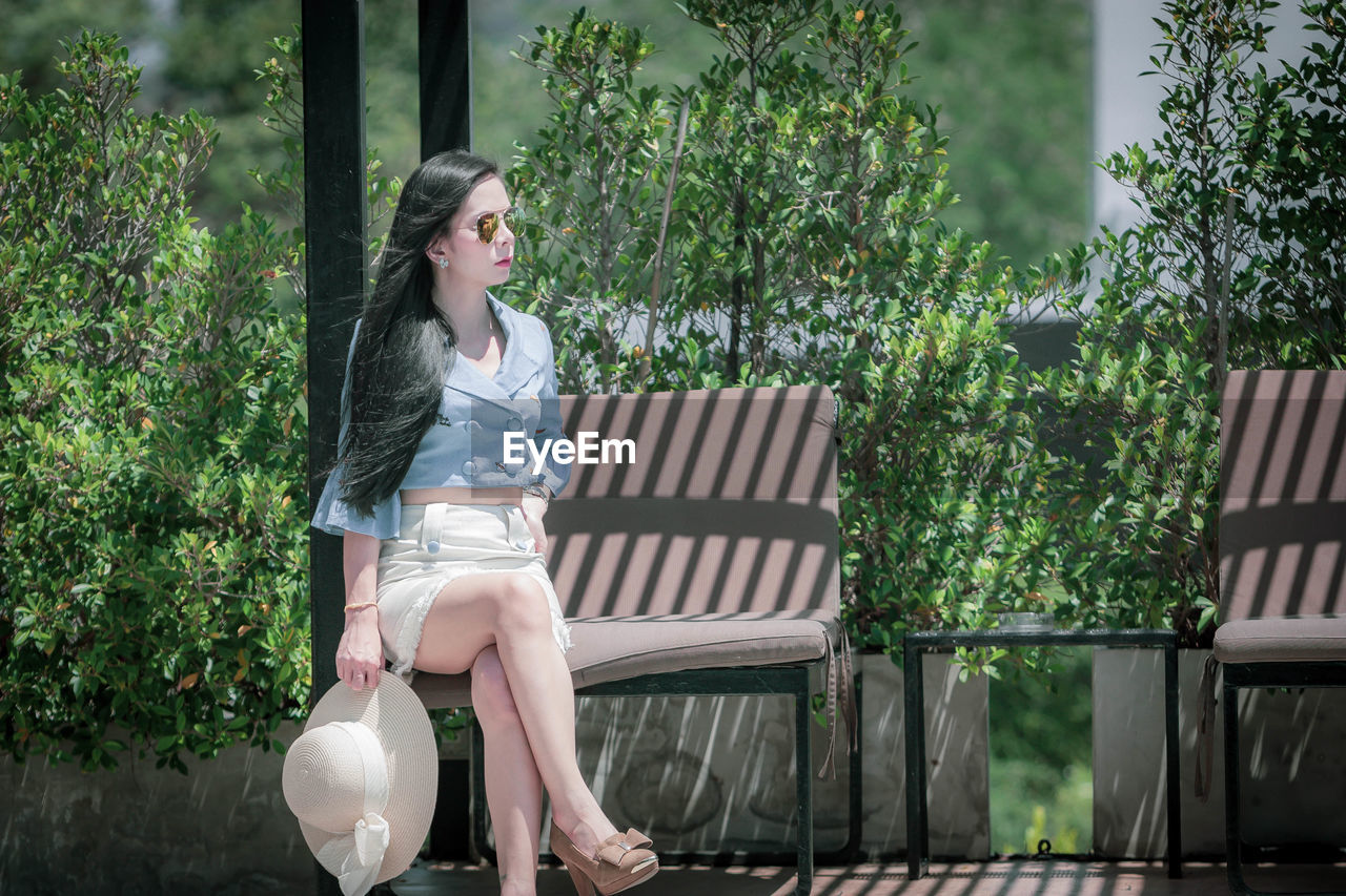 Beautiful woman sitting on bench against trees