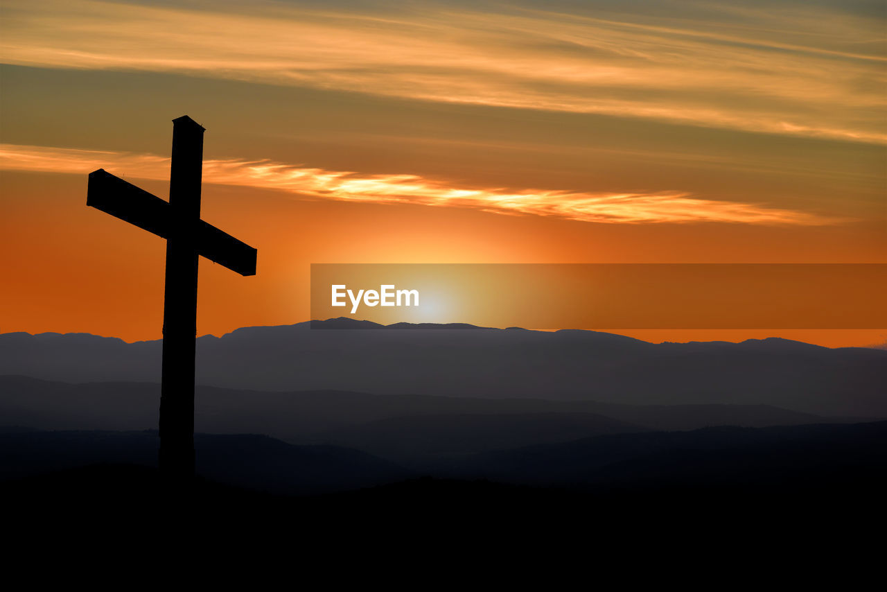 Silhouette cross on mountains against sky during sunset