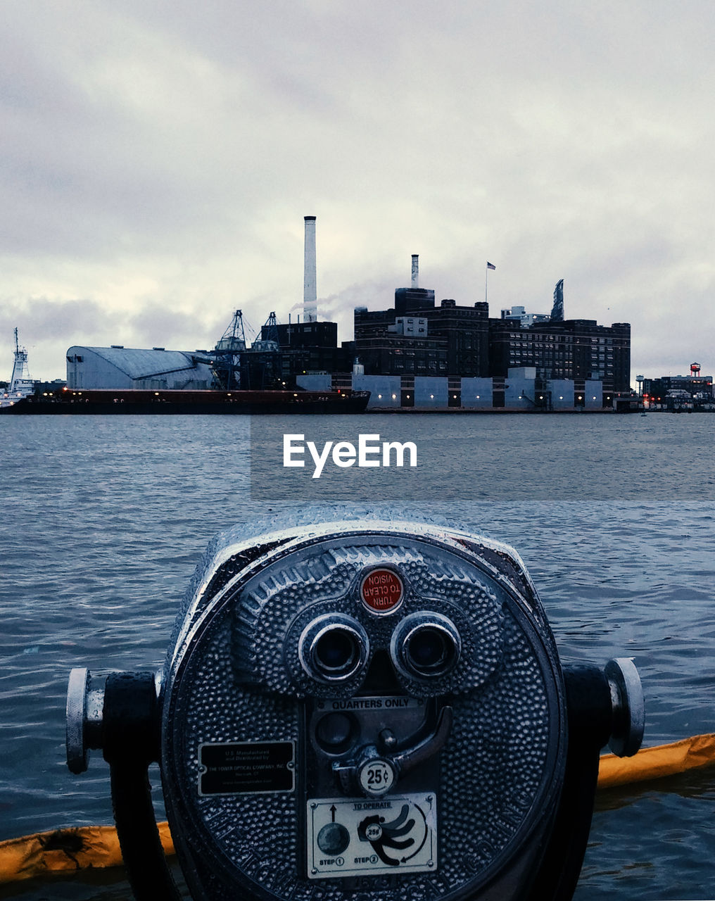 Close-up of coin-operated binoculars by river against buildings and sky