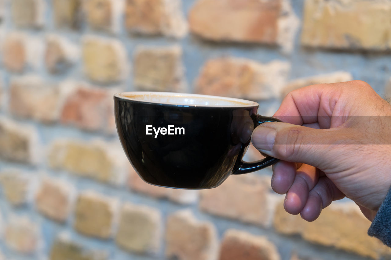 CLOSE-UP OF HAND HOLDING COFFEE CUP AGAINST BLURRED BACKGROUND