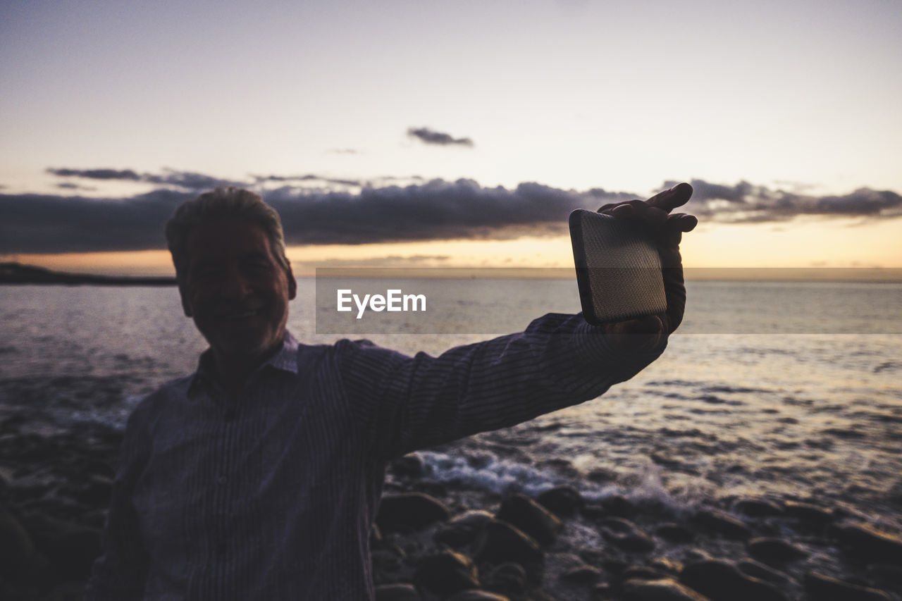 Man photographing from mobile phone at beach during sunset