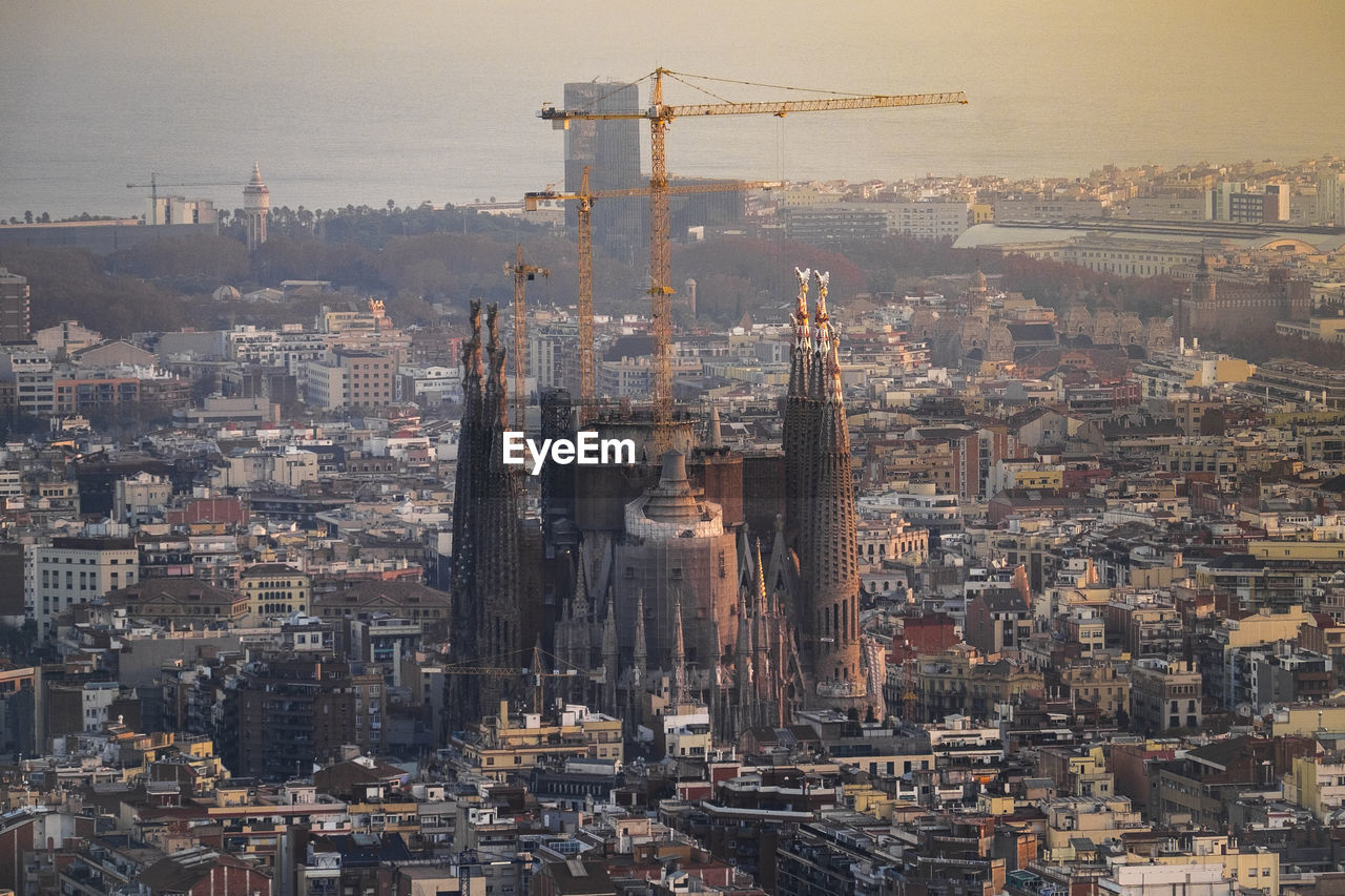 Under construction sagrada familia amidst buildings in city during sunset