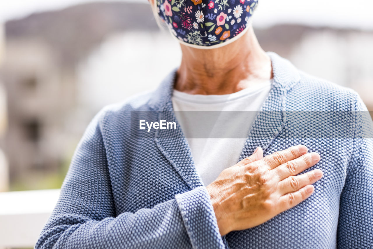 Midsection of senior woman wearing wearing mask gesturing while standing outdoors