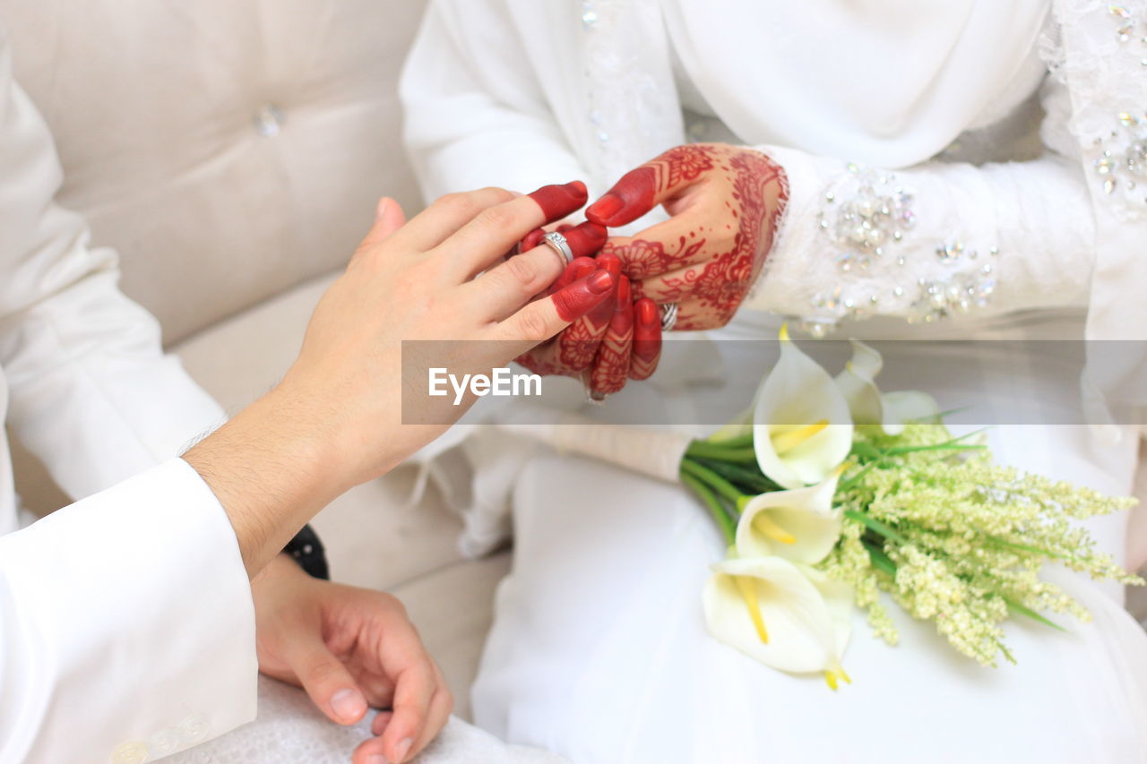 Midsection of bride putting ring in groom finger sitting on sofa during wedding