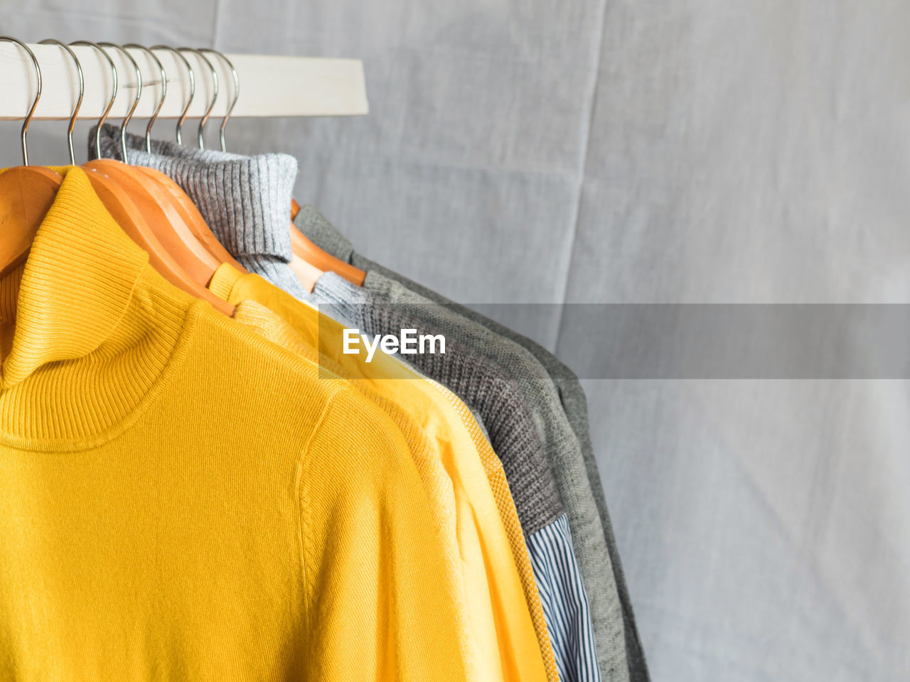 Yellow illuminated color and gray winter sweaters on wooden hangers. trendy fashion cozy clothes.