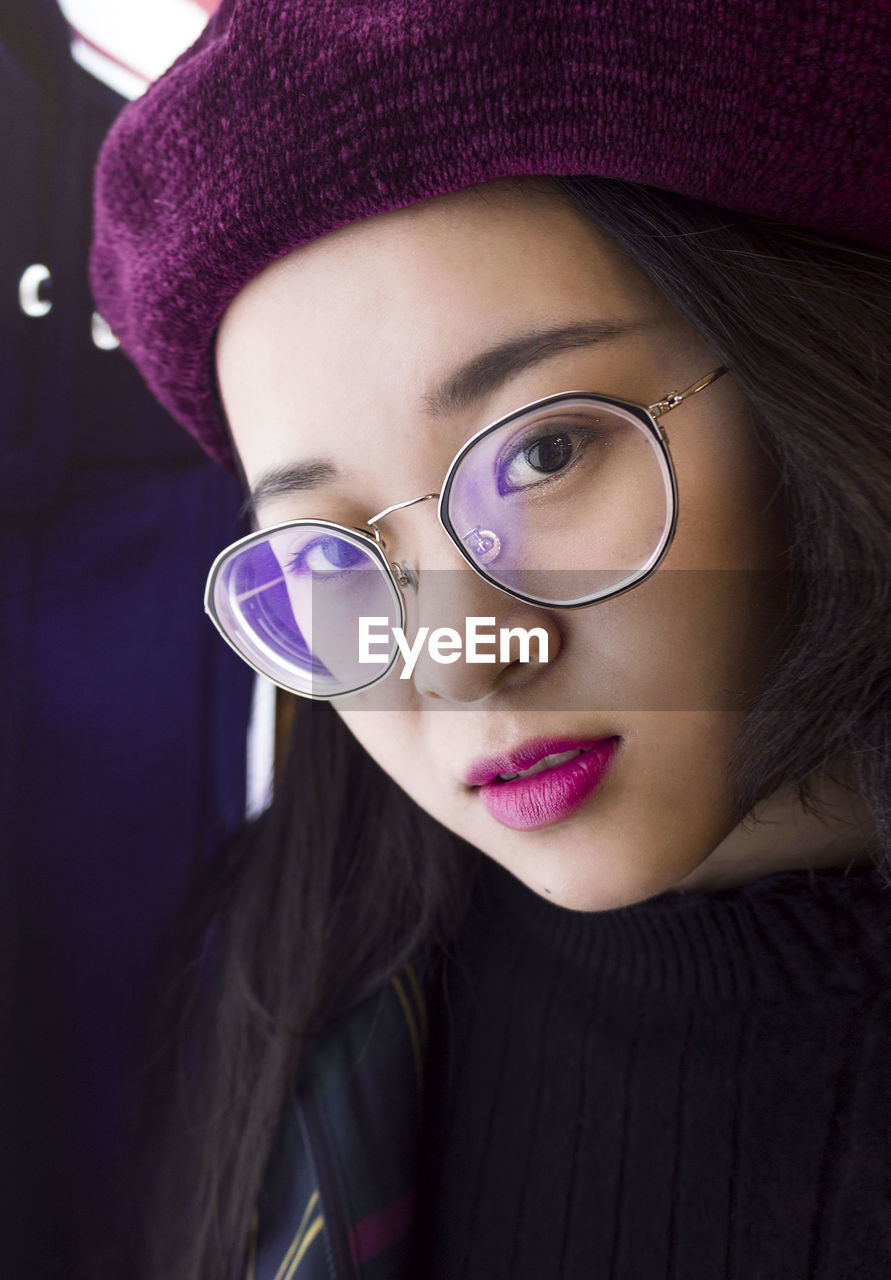 Close-up portrait of young woman wearing hat and eyeglasses