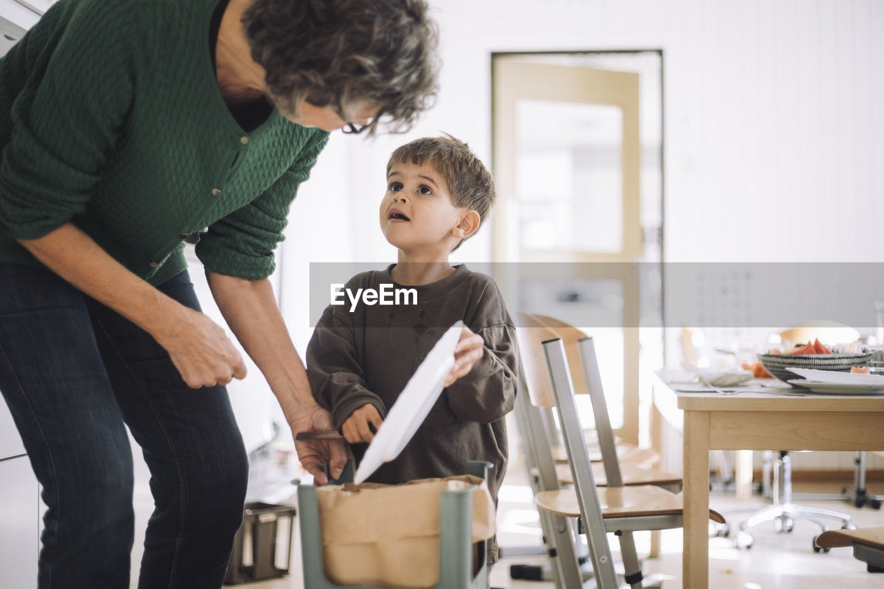 Boy looking at female teacher while throwing food in garbage can at kindergarten