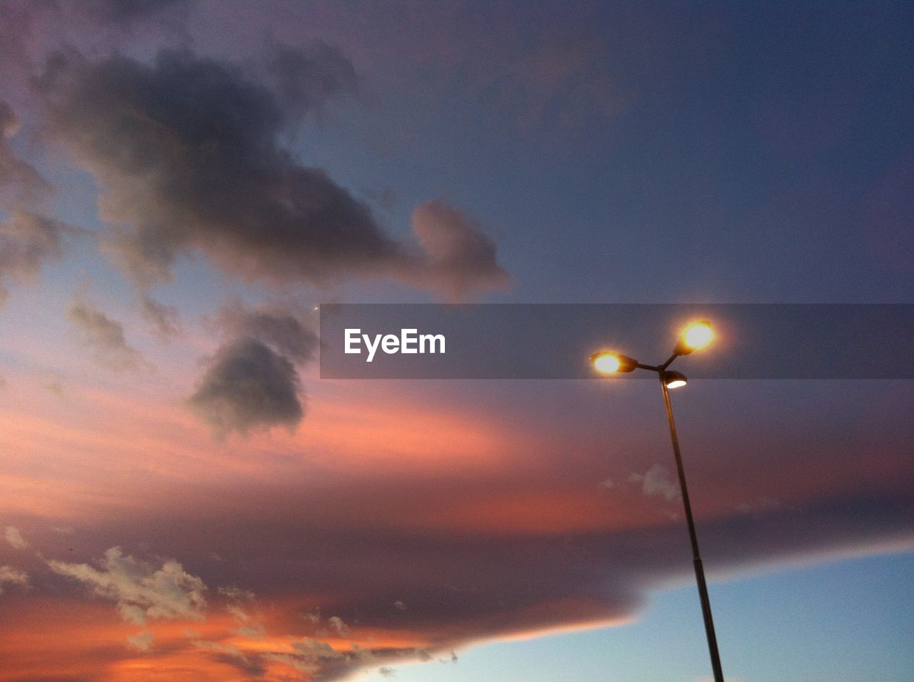 LOW ANGLE VIEW OF ILLUMINATED STREET LIGHTS AGAINST SKY AT SUNSET