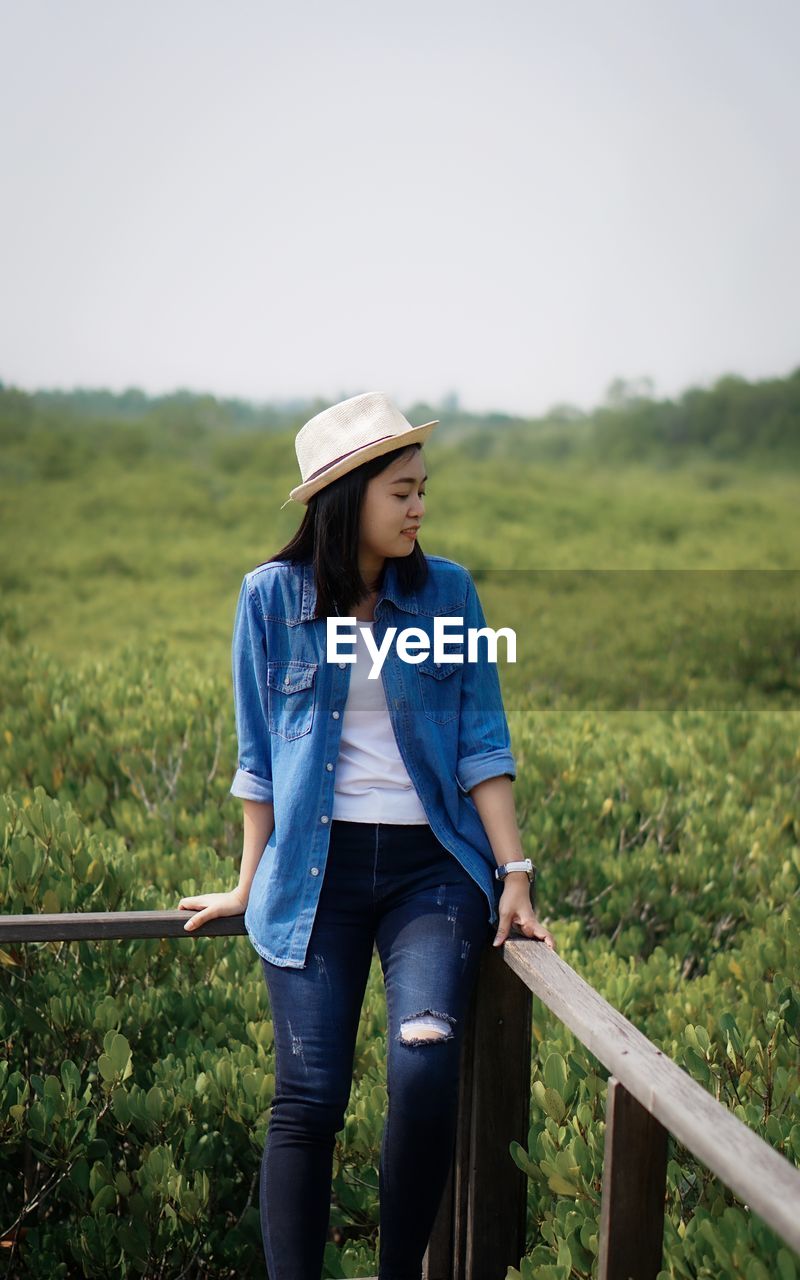 one person, adult, nature, casual clothing, landscape, women, plant, grass, field, sky, clothing, rural scene, agriculture, standing, hat, land, day, environment, three quarter length, leisure activity, front view, young adult, lifestyles, looking, copy space, full length, jeans, person, hairstyle, outdoors, blue, emotion, beauty in nature, looking away, tranquility, female, plain, long hair, farm, non-urban scene, green, rural area, meadow, smiling, relaxation, happiness, trip, tranquil scene, contemplation, scenics - nature, vacation, walking, holiday