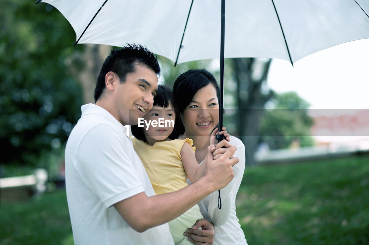 Happy family with white umbrella looking away at park