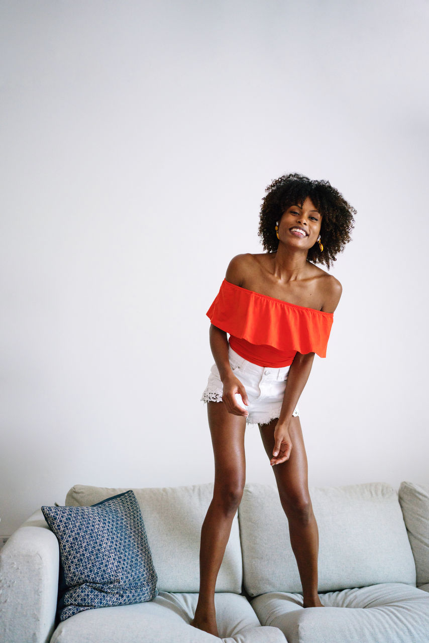 Happy black woman with curly hair having fun jumping dancing on the couch at home