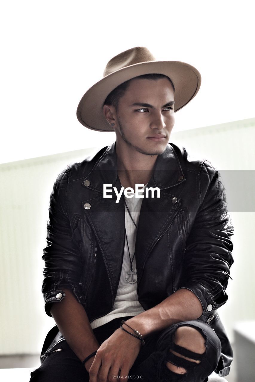 PORTRAIT OF YOUNG MAN WEARING HAT AGAINST GRAY BACKGROUND