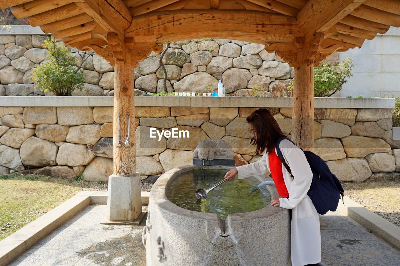 Side view of woman taking water from drinking fountain