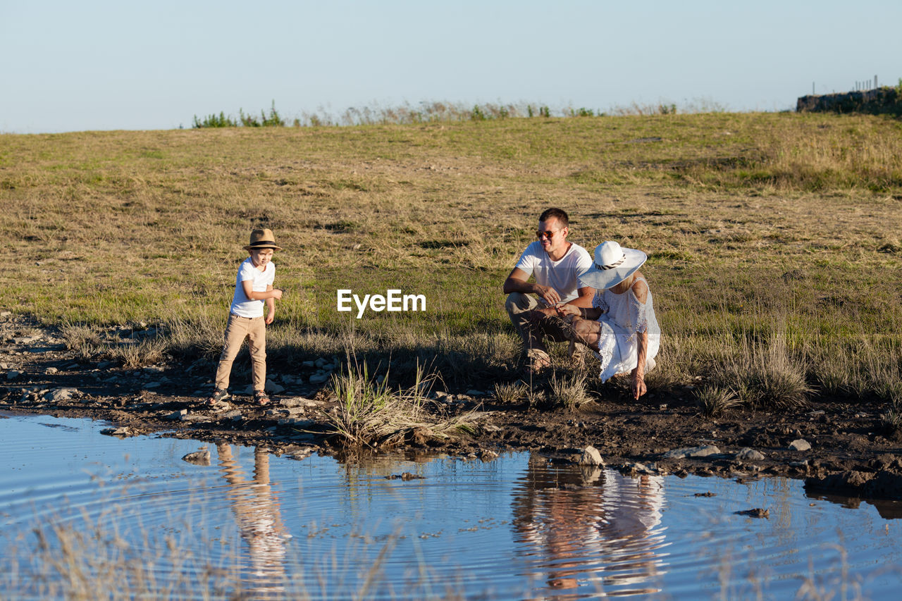 REAR VIEW OF PEOPLE STANDING AT RIVERBANK