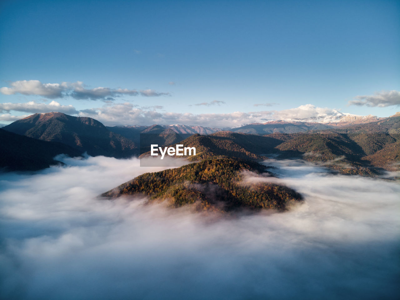 Aerial view, sea of fog and clouds illuminated by the rising sun, snow on the tops of the mountains