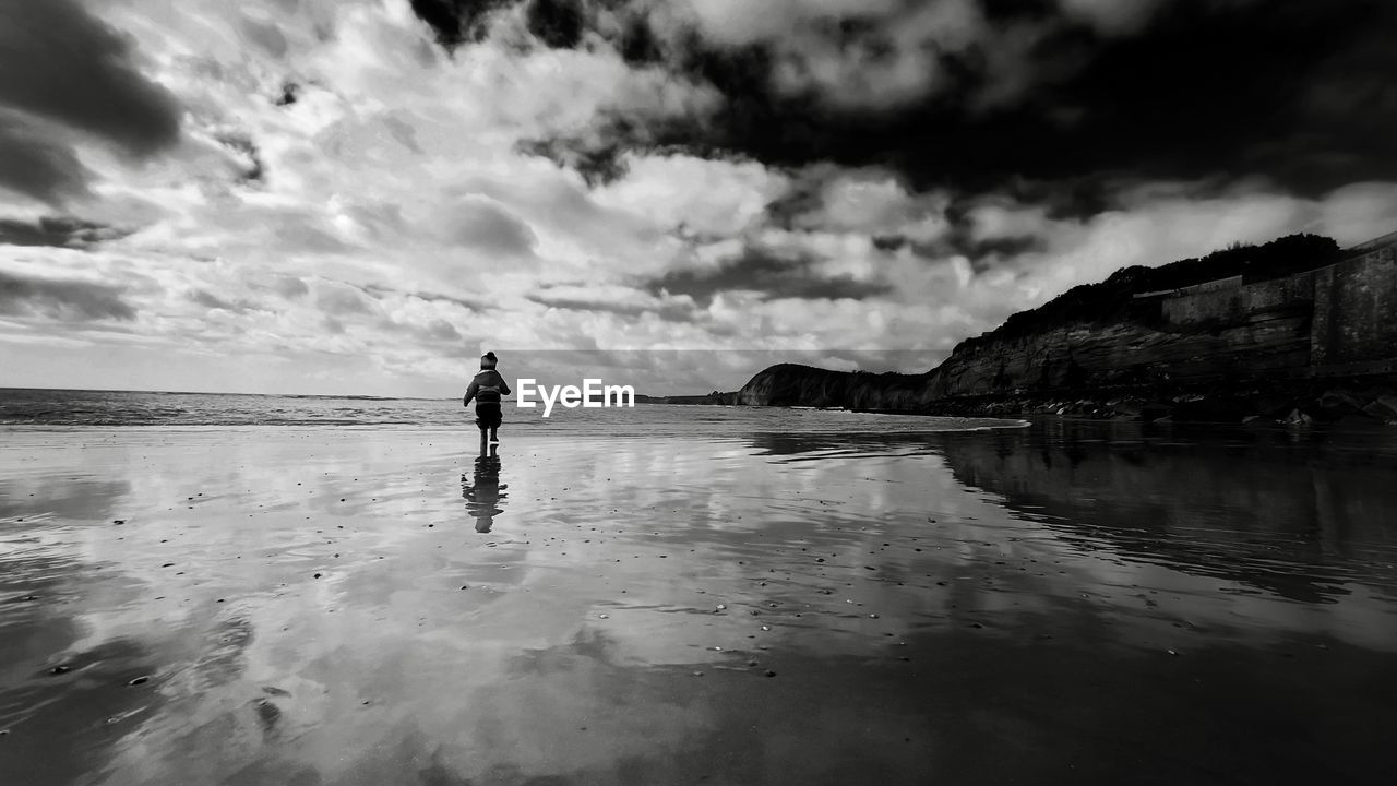 MAN STANDING ON BEACH AGAINST SEA