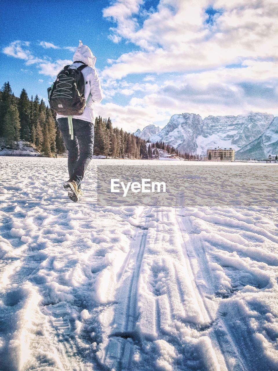 Rear view of person walking on snow covered field against sky