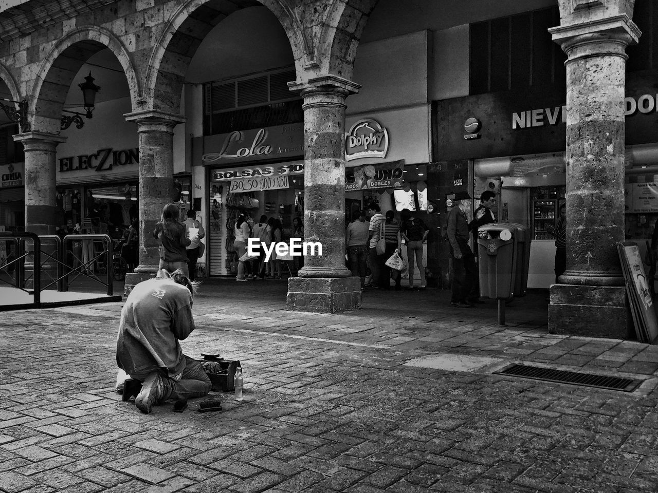 Shoeshiner kneeling in front of stores at city