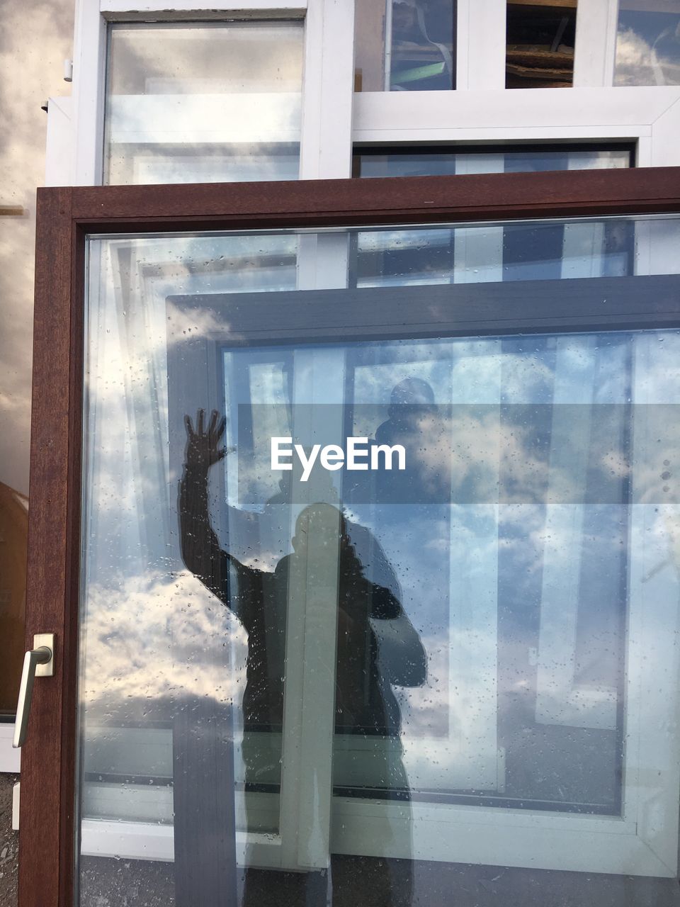 Man with hand raised reflecting on wet glass