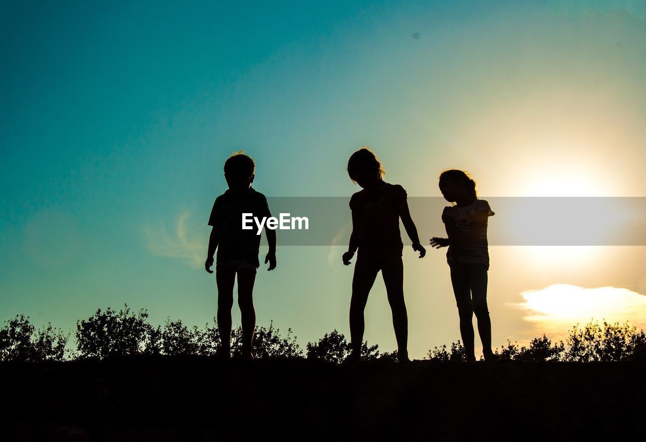 Silhouette children standing in field against sky at dusk