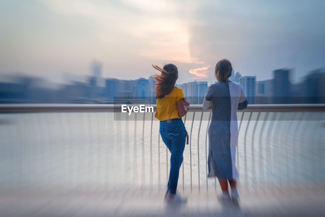 FULL LENGTH OF WOMAN STANDING ON RAILING AGAINST SKY