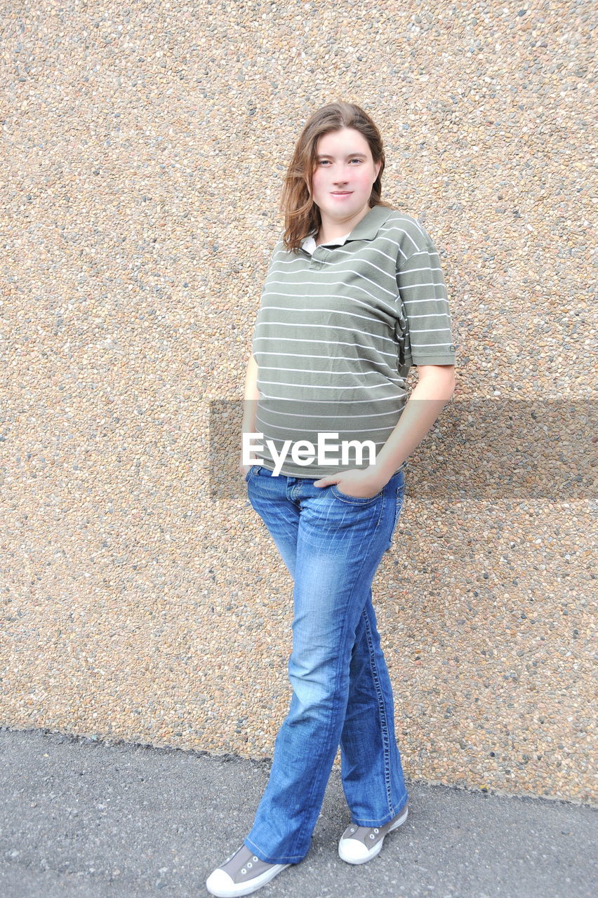 PORTRAIT OF A TEENAGE GIRL STANDING AGAINST STONE WALL