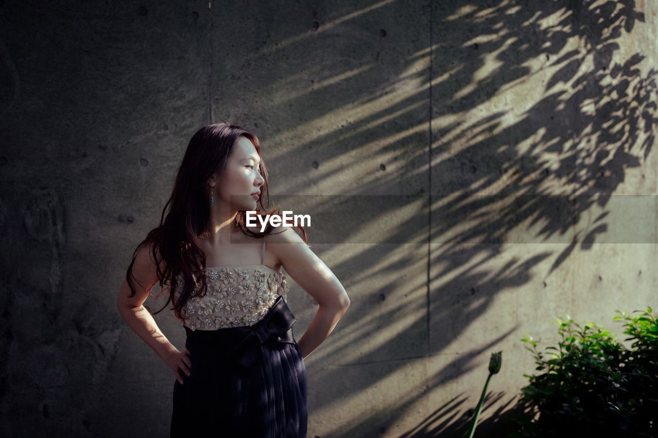 FULL LENGTH OF WOMAN LOOKING AWAY WHILE STANDING AT WATERFALL