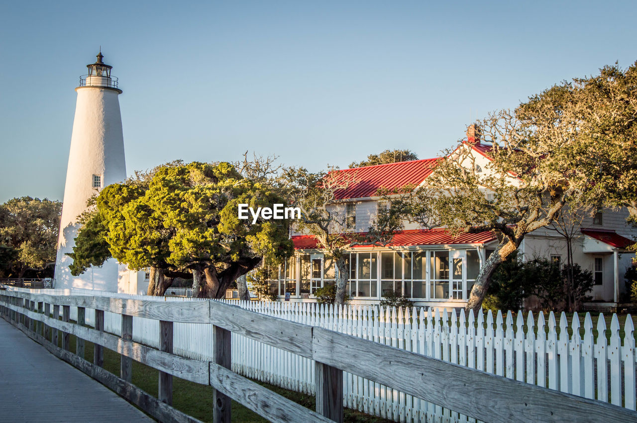 View of lighthouse by building against clear sky