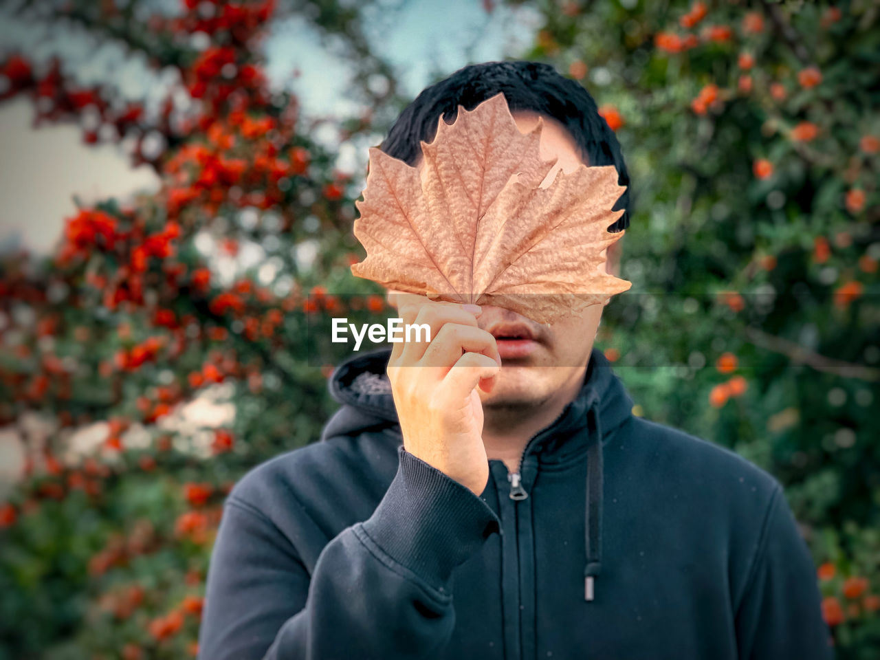 PORTRAIT OF A PERSON STANDING AGAINST PLANTS COVERED WITH LEAVES