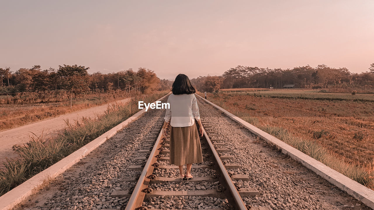 Rear view of woman walking on railroad track against clear sky