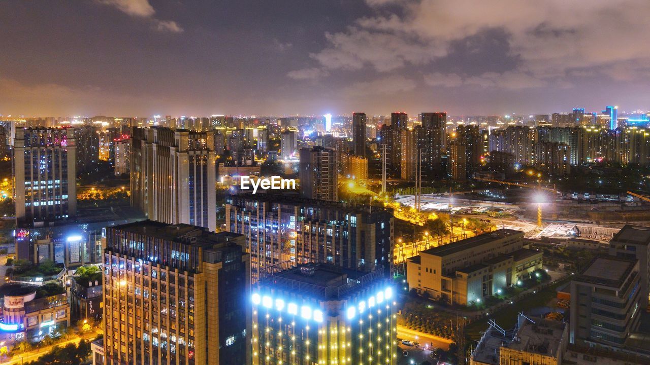 Illuminated modern buildings in city against sky at night