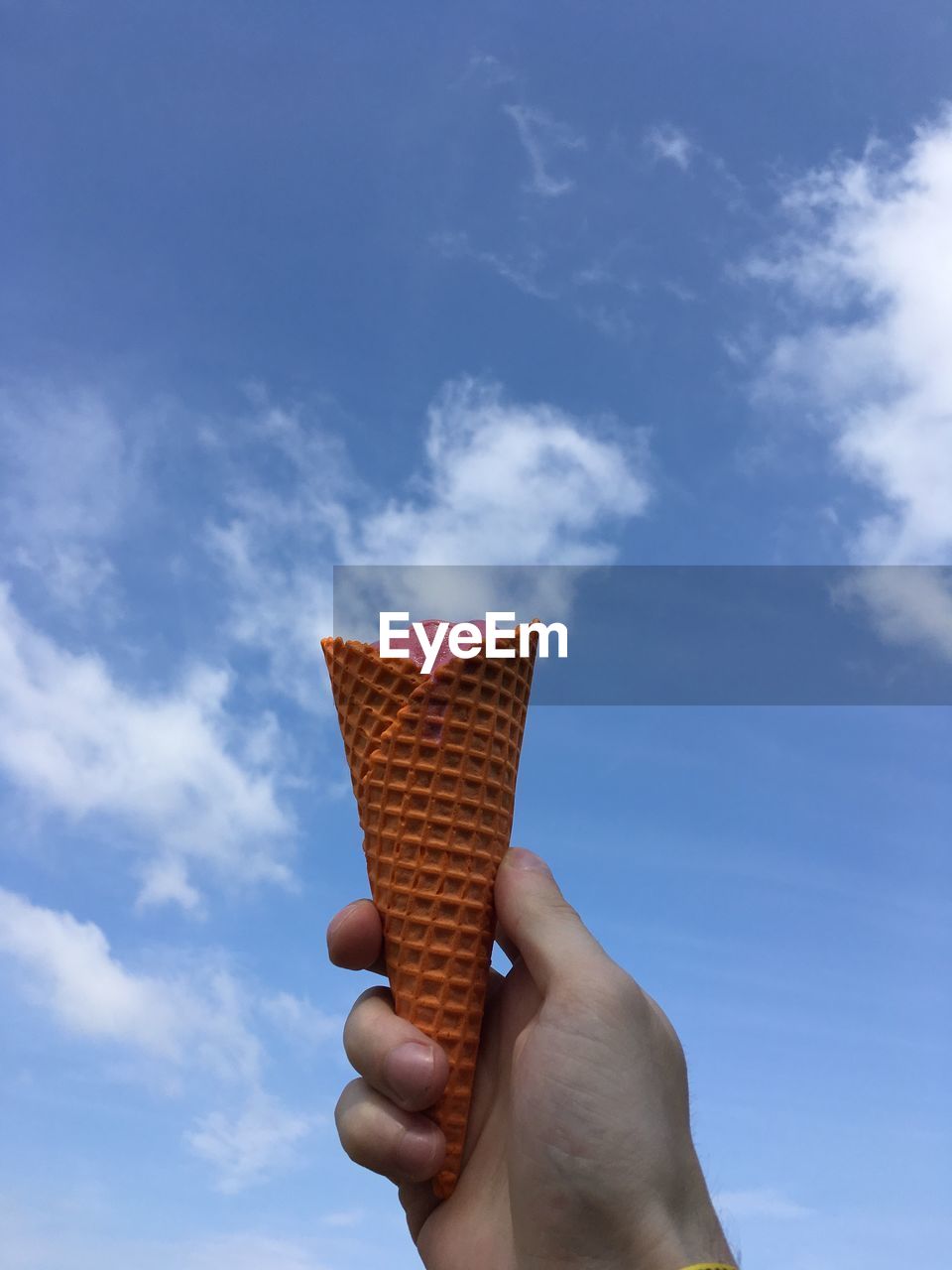 Cropped hand of person holding ice cream cone against sky