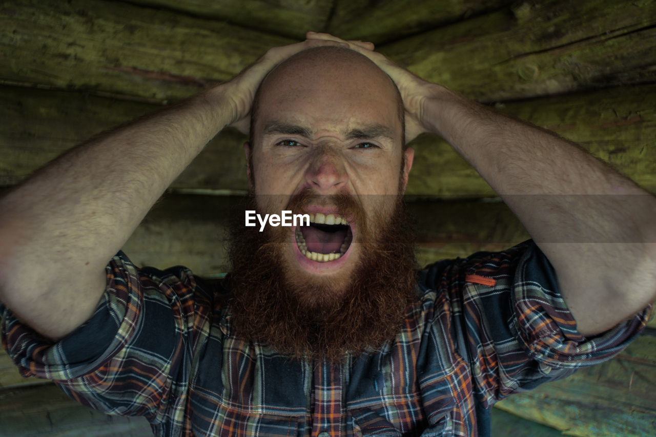 Close-up portrait of frustrated bald man screaming in log cabin