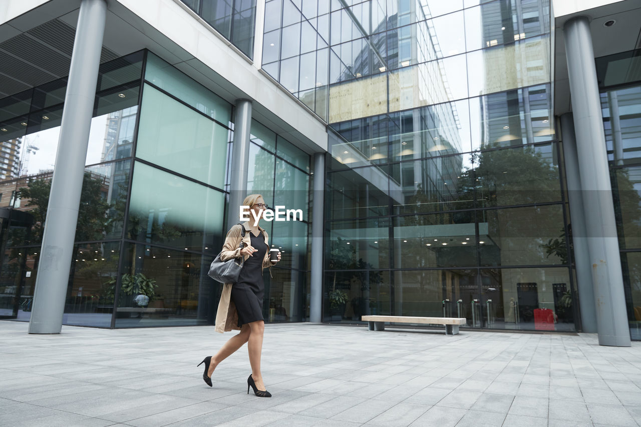 Woman holding coffee cup while walking against office building