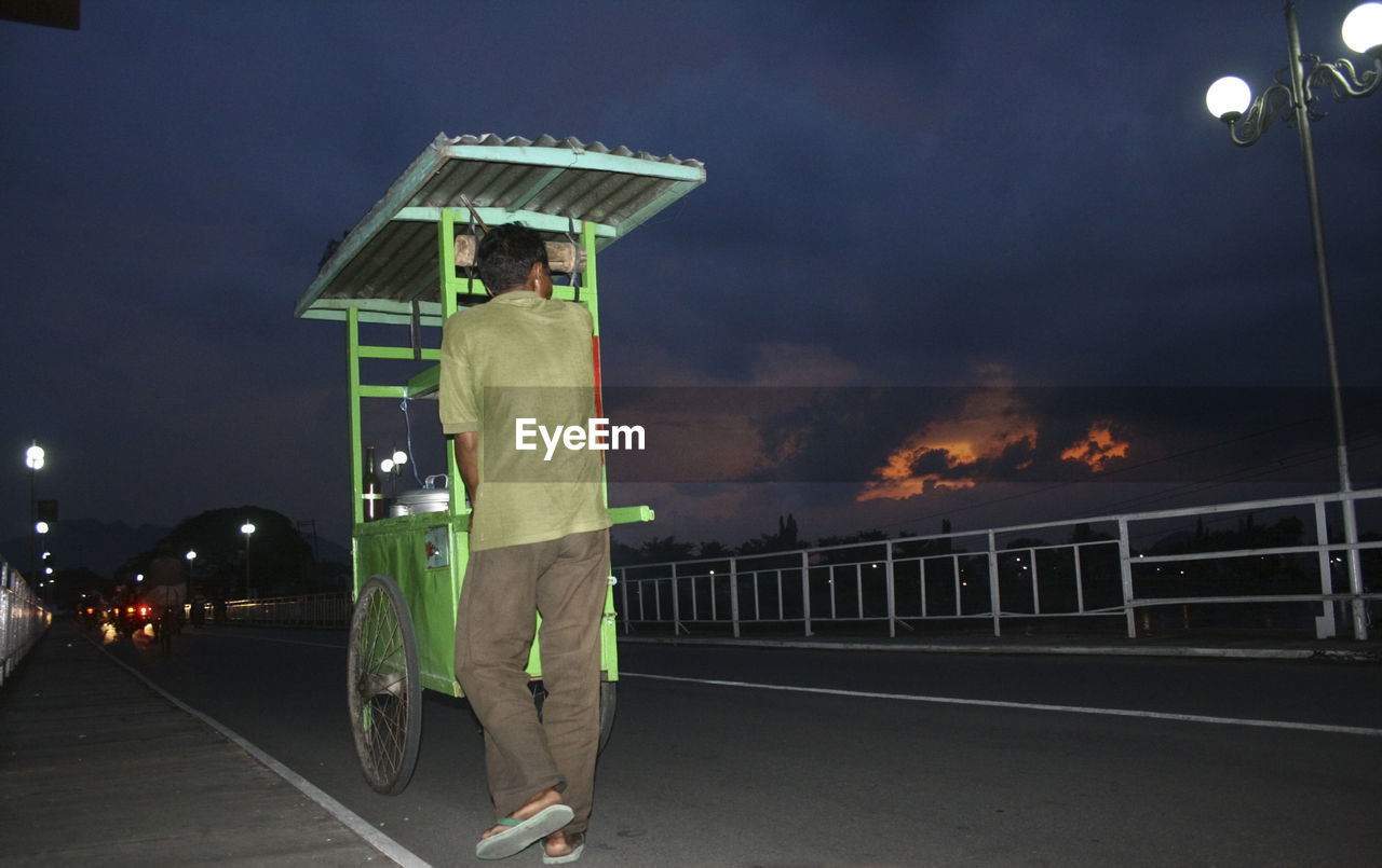 night, one person, full length, adult, men, transportation, sky, sign, standing, architecture, person, clothing, protection, nature, illuminated, street, street light, city, fire, burning, road, sports, security, motion, outdoors